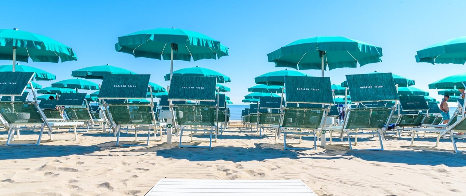 Ombrelloni verdi su spiaggia dorata, sole splendente, mare invitante.