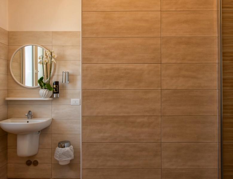 Elegant bathroom with beige tiles, round mirror, and decorative flower.