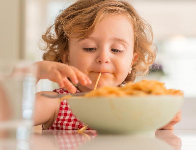 Bambina felice mangia spaghetti con gioia e curiosità.