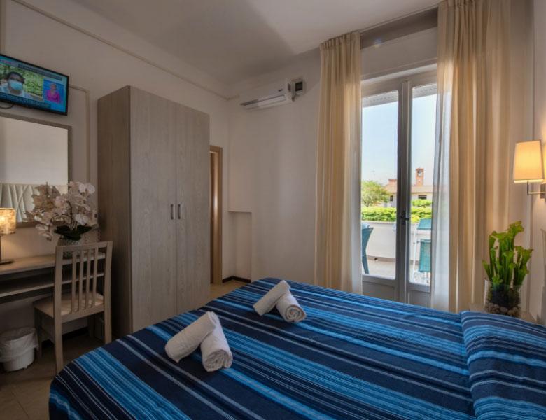 Camera accogliente con letto blu, balcone soleggiato, atmosfera rilassante.