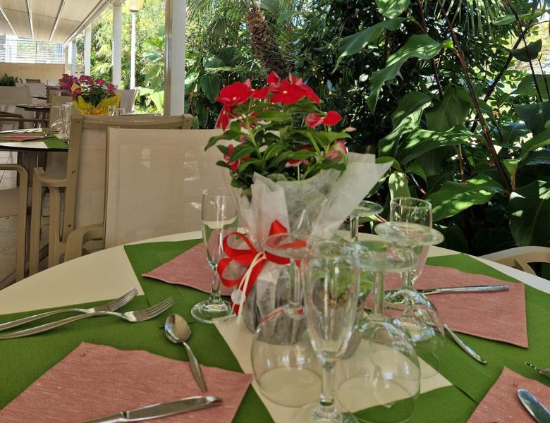 Ristorante all'aperto, tavoli eleganti, fiori vivaci, verde rigoglioso, atmosfera rilassante e accogliente.