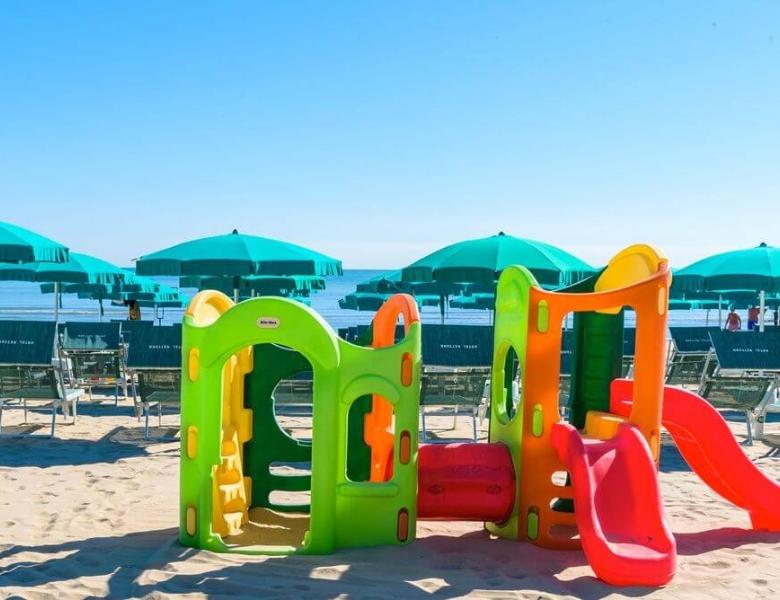 Giochi colorati su sabbia dorata, mare calmo e ombrelloni verdi.