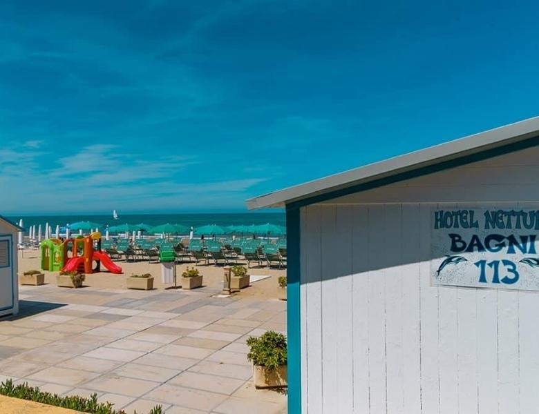 Spiaggia luminosa, ombrelloni verdi, cielo azzurro, giochi colorati, mare calmo.